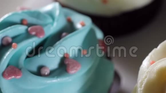 滑动相机拍摄在马芬上涂上蓝色和白色奶油把糖筛在粉红色的糖霜蛋糕上视频的预览图