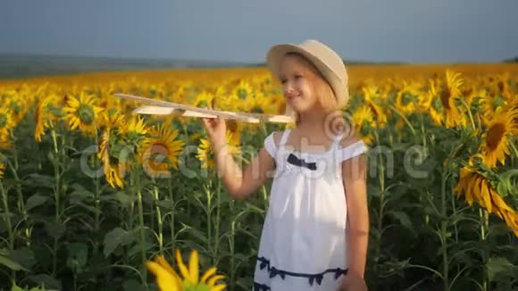 戴帽子的女孩玩木飞机快乐的孩子在日落时在向日葵田玩玩具飞机在视频的预览图