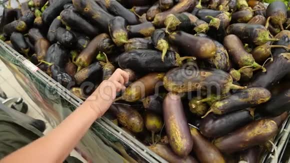 一个女人在蔬菜货架上的超市里买蔬菜和水果一个人从腐烂的地方选择茄子视频的预览图