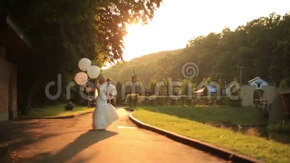 快乐的新婚夫妇在夕阳下的金秋公园里拿着气球散步一起玩得开心视频的预览图