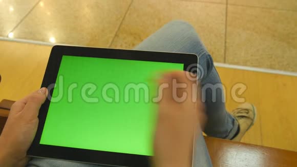 年轻女孩坐在购物中心的长凳上用平板电脑工作女性手使用平板电脑绿色屏幕视频的预览图