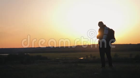 一个带背包的剪影青年游客使用手机在夕阳的光芒中慢动作旅费视频的预览图