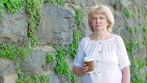 喝咖啡的老年妇女背景中野生石头的复古墙视频的预览图