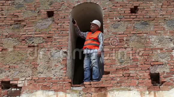 建筑工人在旧墙附近用smarth电话拍照视频的预览图