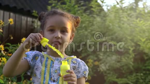 一个快乐的小白种人女孩在阳光明媚的日子里缓慢地吹着肥皂泡童年快乐或儿童概念视频的预览图