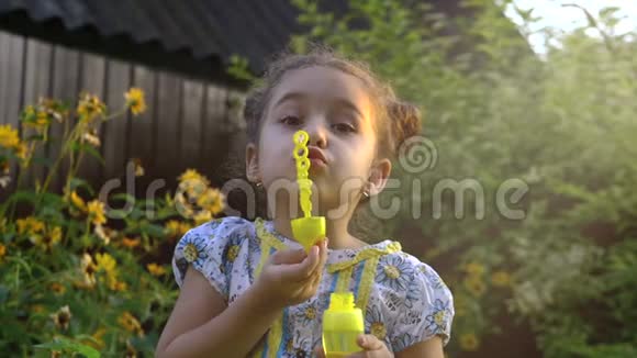 一个快乐的小白种人女孩在阳光明媚的日子里缓慢地吹着肥皂泡童年快乐或儿童概念视频的预览图