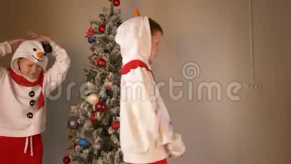 可爱的男孩穿着圣诞老人和雪人的节日服装用球和花环装饰圣诞树视频的预览图