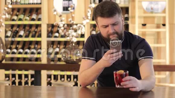在餐馆或咖啡馆喝红饮料的男人在喝红鸡尾酒时使用智能手机的年轻人视频的预览图