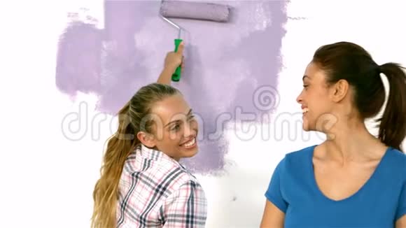 漂亮的女孩用画笔和另一个女孩微笑着画墙视频的预览图