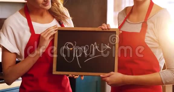 两个微笑的女服务员举着一块开放的招牌视频的预览图