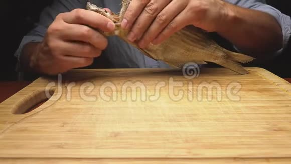 特写镜头男性手清洁咸干鱼在切割板上4K慢动作视频的预览图