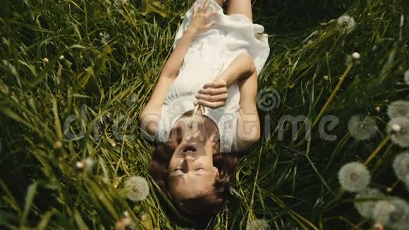美丽的女孩在阳光明媚的草地上吹着蒲公英视频的预览图