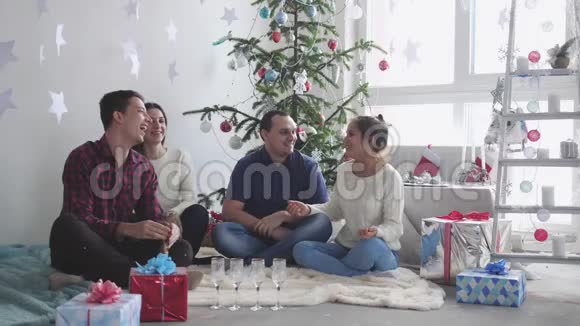 庆祝圣诞节的年轻快乐的朋友正坐在圣诞树前玩得开心庆祝新概念视频的预览图