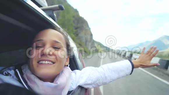 微笑着年轻的黑发女人在一辆车里玩风开车经过美丽的山脉3840x2160视频的预览图