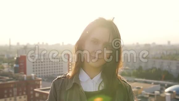 年轻漂亮的女人站在高层建筑的屋顶上看着夕阳看着镜头慢节奏视频的预览图