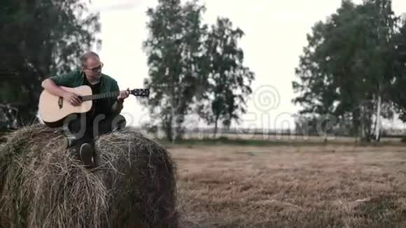 穿着格子衬衫的人在干草堆上坐在田里弹吉他视频的预览图