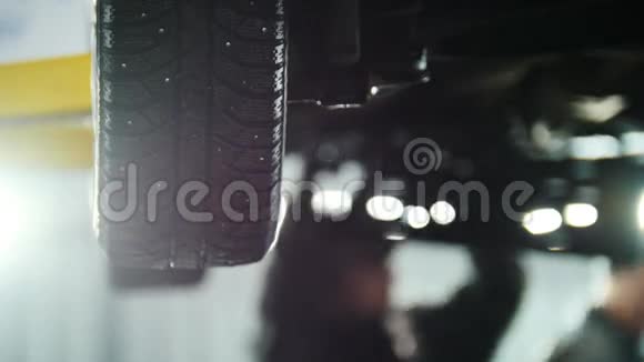 汽车服务机械师在提升的汽车车轮下工作时松开汽车装置视频的预览图