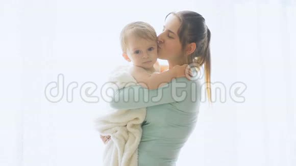 快乐的年轻母亲在窗口搂着她的小儿子的慢镜头视频的预览图