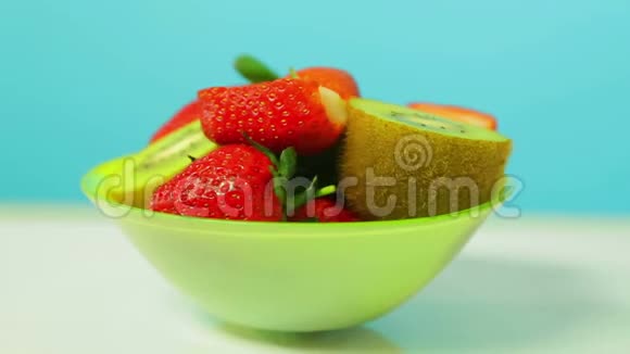 鲜果猕猴桃和绿色盘子上蓝色背景的草莓片旋转成一圈视频的预览图