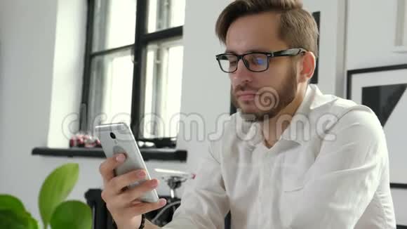 同事的好消息自信的年轻人穿着智能休闲装拿着智能手机坐着看着它视频的预览图