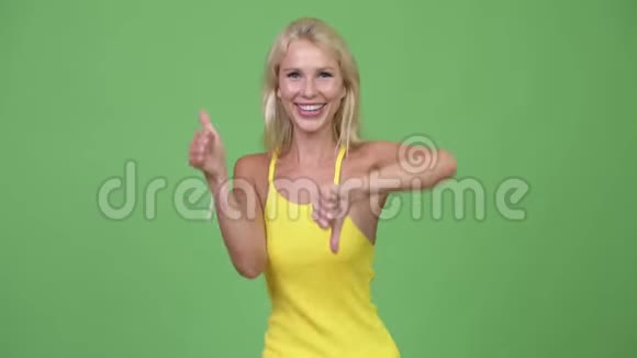 年轻迷茫的金发美女在竖起大拇指和大拇指之间做出选择视频的预览图
