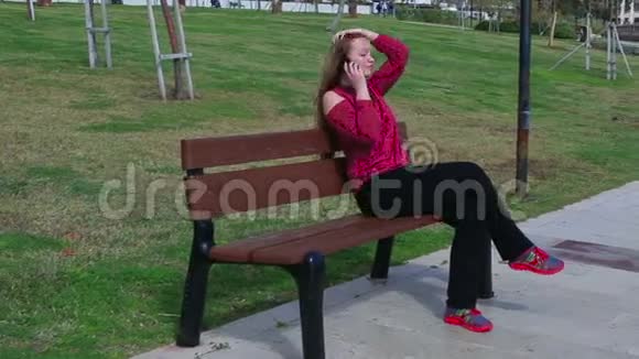 夏天美丽的少女坐在公园的长椅上一边用智能手机聊天视频的预览图