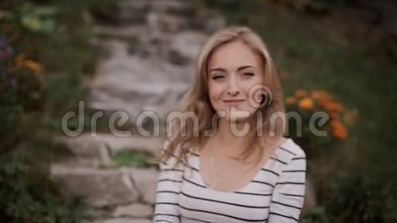 花园里一个微笑的女孩坐在楼梯上的画像视频的预览图