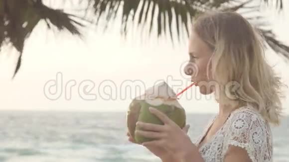日落时分在海滩上喝椰子的女人视频的预览图