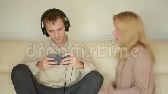 女人用耳机对男人大喊大叫丈夫在智能手机上玩视频的预览图