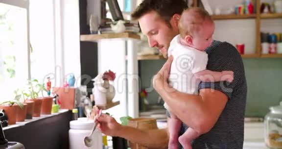父亲在厨房里抱着婴儿做饭视频的预览图