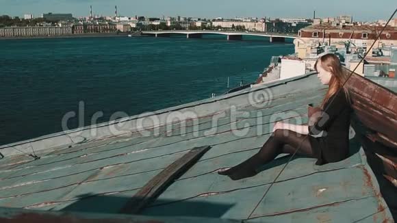 穿着黑色裙子坐在风景优美的城市景观屋顶上的漂亮女孩视频的预览图