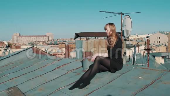 美丽的少女穿着黑色连衣裙坐在屋顶上风景优美的城市景观视频的预览图