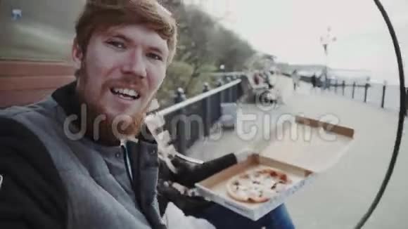 一对夫妇在海滨吃披萨天气寒冷在一起年轻人穿着夹克女人穿着外套坐在长凳上视频的预览图