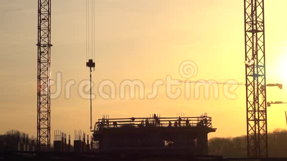 吊车和施工现场工人在橙色日落时的剪影4K视频的预览图