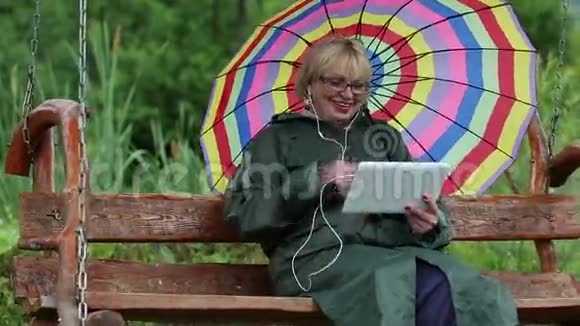 女人坐在秋千凳上穿着绿色雨衣带着多色伞视频的预览图