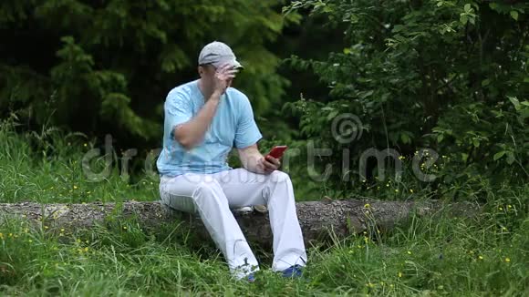 男人坐在原木上拿着电话微笑着调整帽子视频的预览图