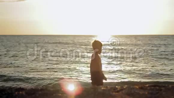 小男孩在日落时呆在平静的大海里视频的预览图