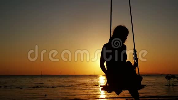 热带海滩上美丽的日落年轻女子在秋千上荡秋千慢动作视频的预览图