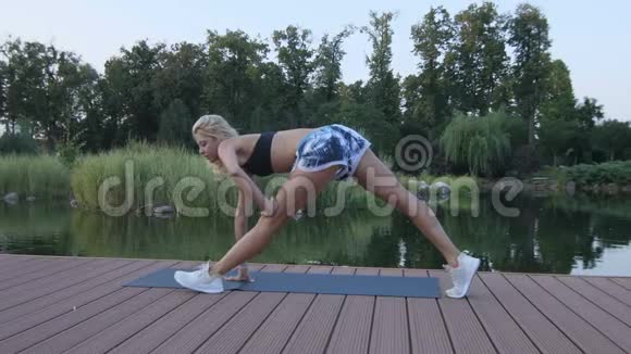 日落时分一个金发的运动女孩正忙着在池塘边伸展视频的预览图
