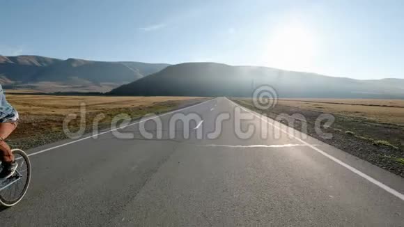 男人骑着自行车在沥青路上朝阳光明媚的日落天空20s4k视频的预览图