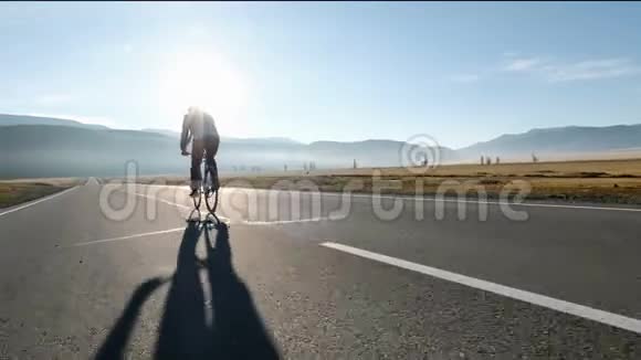男人骑着自行车在沥青路上朝阳光明媚的日落天空20s4k视频的预览图