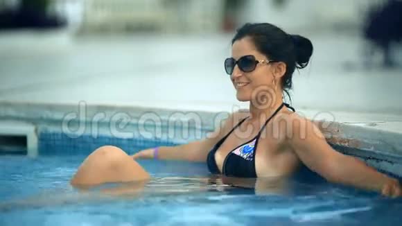 美丽的黝黑女人穿着比基尼在游泳池里放松戴着太阳镜视频的预览图