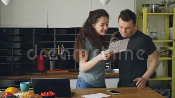 一对漂亮的幸福夫妇在家吃早餐时在厨房里收到一封正在展开的好消息视频的预览图