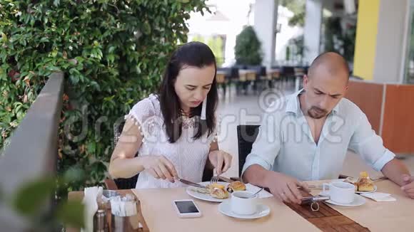 年轻夫妇在户外咖啡馆的一张桌子上吃早餐和聊天视频的预览图