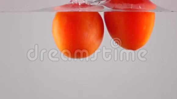 超级慢动作红色成熟的西红柿在水中落下漂浮灰色背景视频的预览图