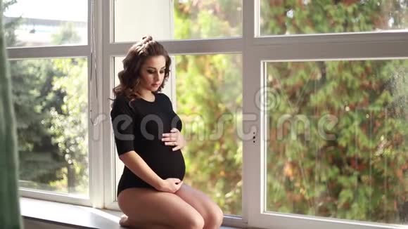 孕妇坐在大窗户前穿着黑色紧身衣的模特她把手放在肚子上快乐的未来视频的预览图