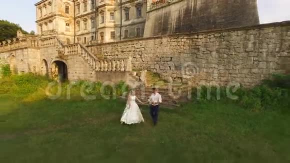 鸟瞰美丽的婚礼情侣在古色古香的城堡前漫步4k视频的预览图