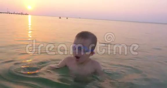 太阳下山时戴护目镜的小孩在海上玩视频的预览图
