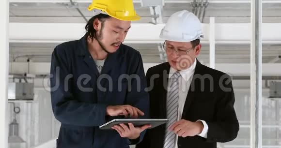 年轻的亚洲工程师用平板电脑向工业工厂的高级执行工程师展示他的工作视频的预览图