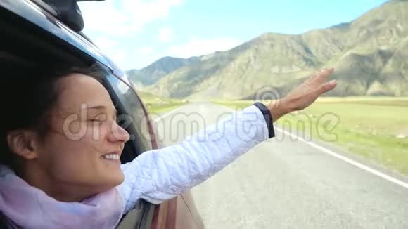 微笑着年轻的黑发女人在一辆车里玩风开车经过美丽的山脉3840x2160视频的预览图
